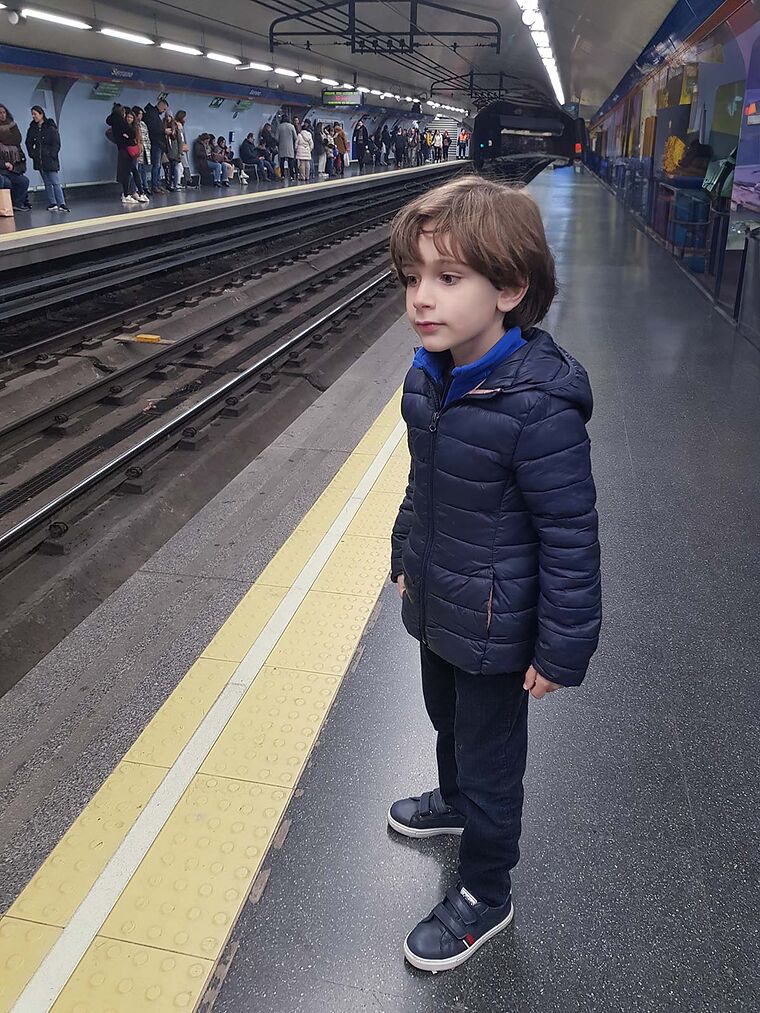 Nico de pie en el andén de una estación de metro esperando a que llegue el tren