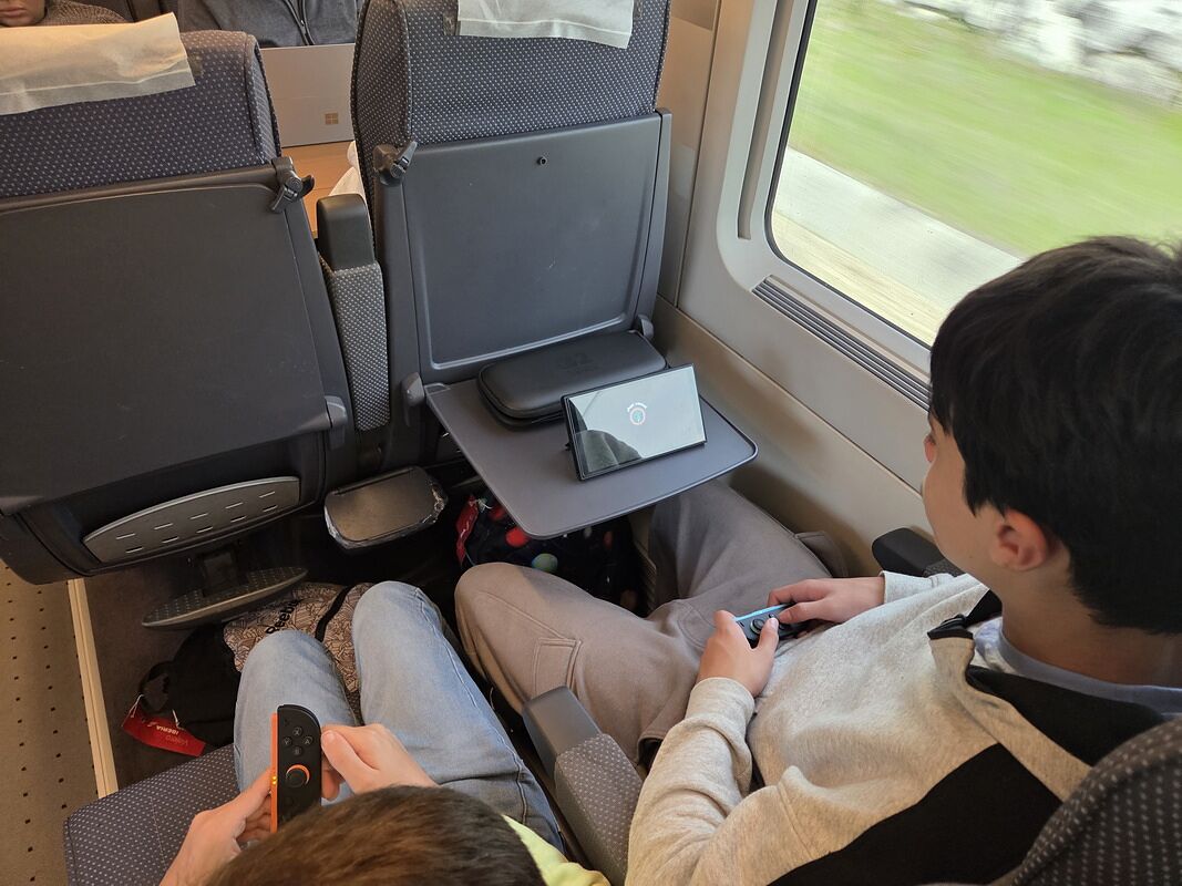 Nico y Bruno jugando a la consola dentro del AVE, con el paisaje pasando movido por la ventanilla
