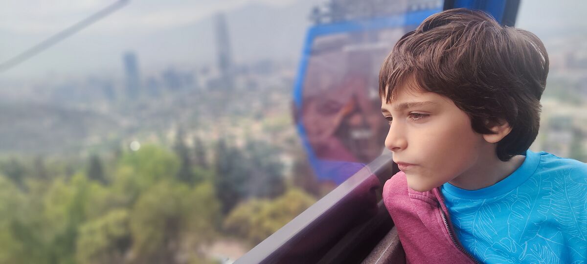 Nico mirando Santiago de Chile desde dentro de una cabina del teleférico, con la torre Costanera al fondo entre la bruma