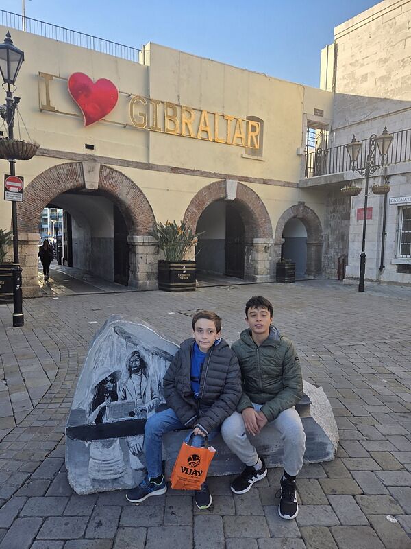 Nico y Bruno sentados en una piedra bajo el cartel de I love Gibraltar, en la plaza Casemates