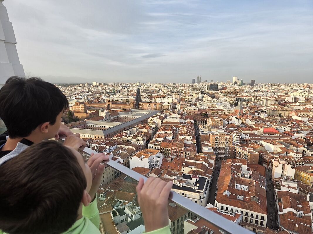 Nico y Bruno asomados a una barandilla mirando Madrid entero desde un mirador en altura, con los tejados rojos hasta el horizonte