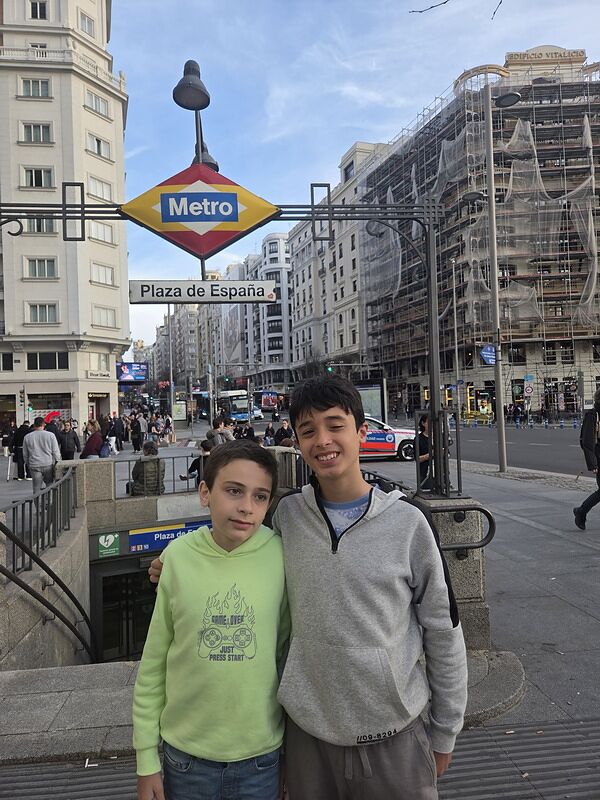 Nico y Bruno bajo el rótulo del Metro de Madrid en la boca de Plaza de España, con la Gran Vía al fondo