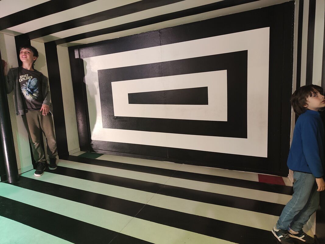 Nico y Bruno en la sala de ilusiones ópticas de rayas blancas y negras, uno parece mucho más alto que el otro