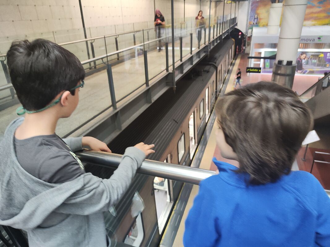 Nico y Bruno asomados a la barandilla viendo llegar un tren del subte de Buenos Aires al andén de abajo